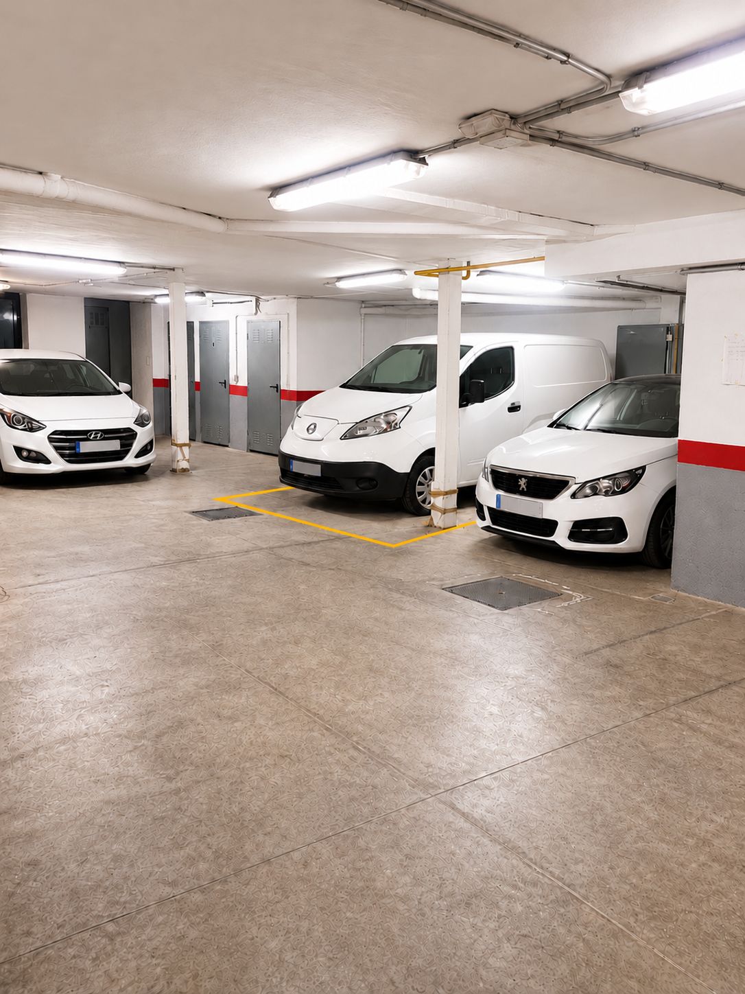 Ett parkeringsgarage med tre vita fordon parkerade på anvisade platser.
