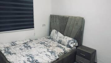 Un lit simple avec une tête de lit, une commode de chevet et une fenêtre avec des stores.
