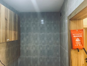 Un bagno con piastrelle grigie, una porta in legno e una coperta antincendio appesa al muro.