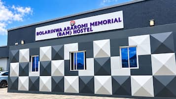 Un edificio con un'insegna che indica 'Bolarinwa Araromi Memorial (BAM) Hostel', caratterizzato da una facciata geometrica e due finestre.