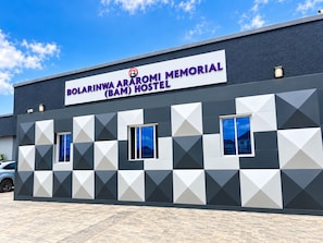 Un edificio con un'insegna che indica 'Bolarinwa Araromi Memorial (BAM) Hostel', caratterizzato da una facciata geometrica e due finestre.