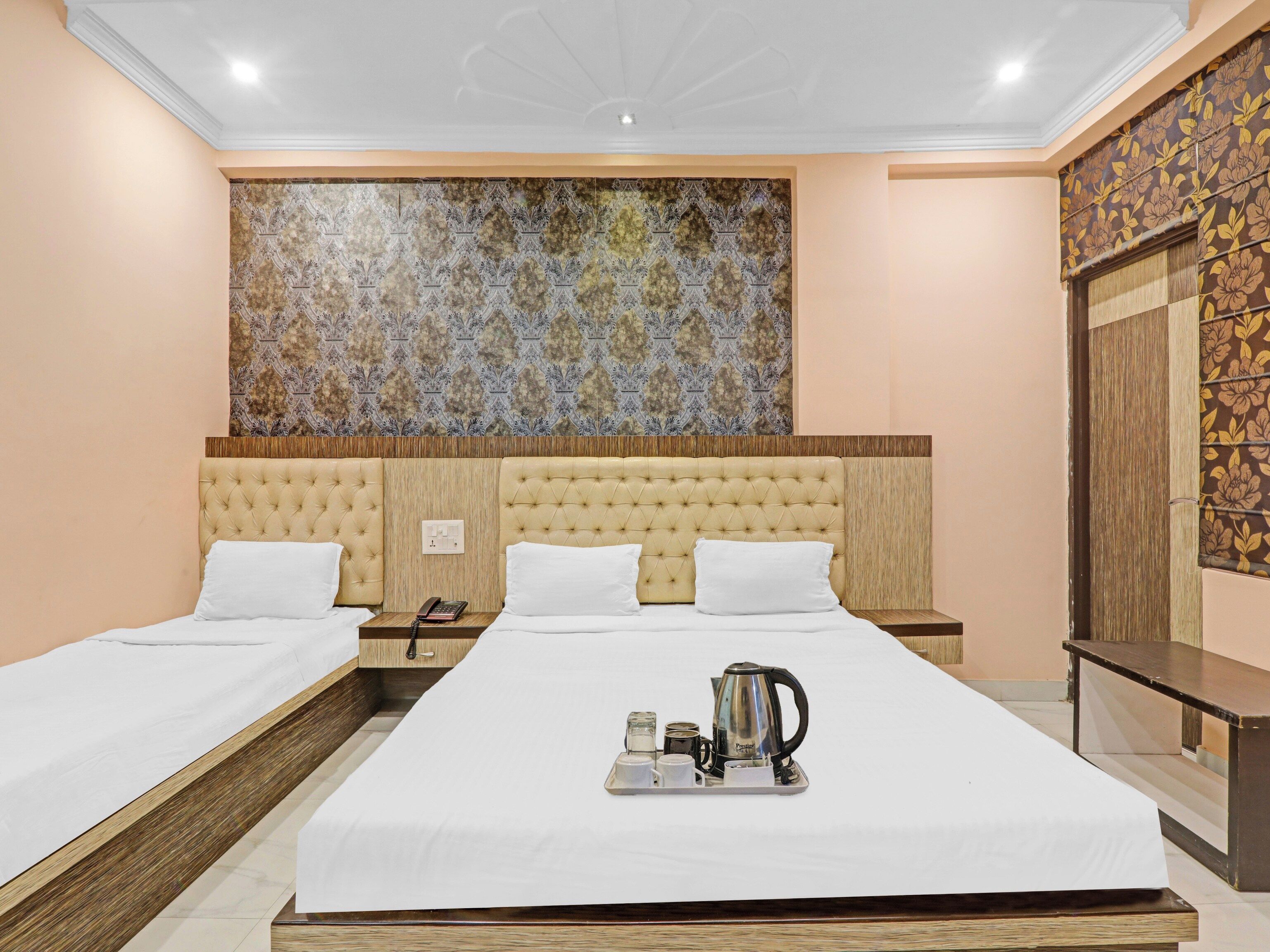A hotel room with two beds, a large decorative wall, a wooden headboard, and a tray with a kettle and cups.