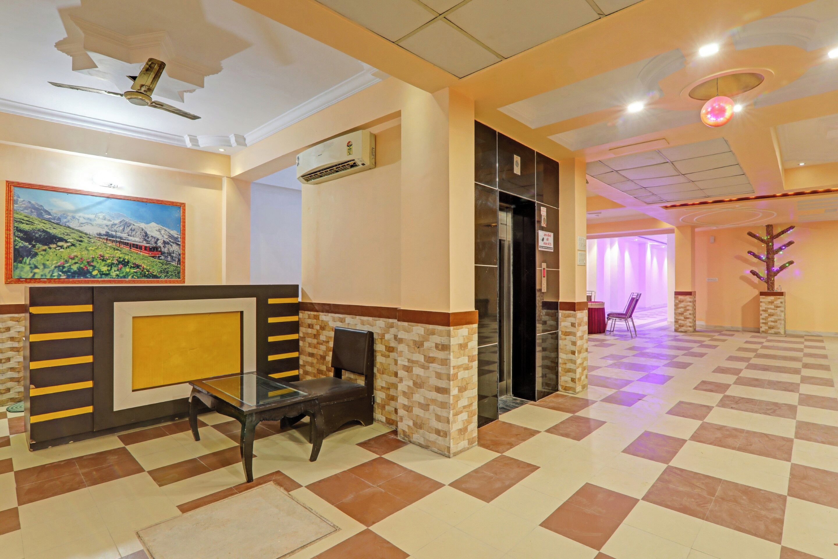 A hotel lobby with a checkered floor, a reception desk, a painting, and a ceiling fan.