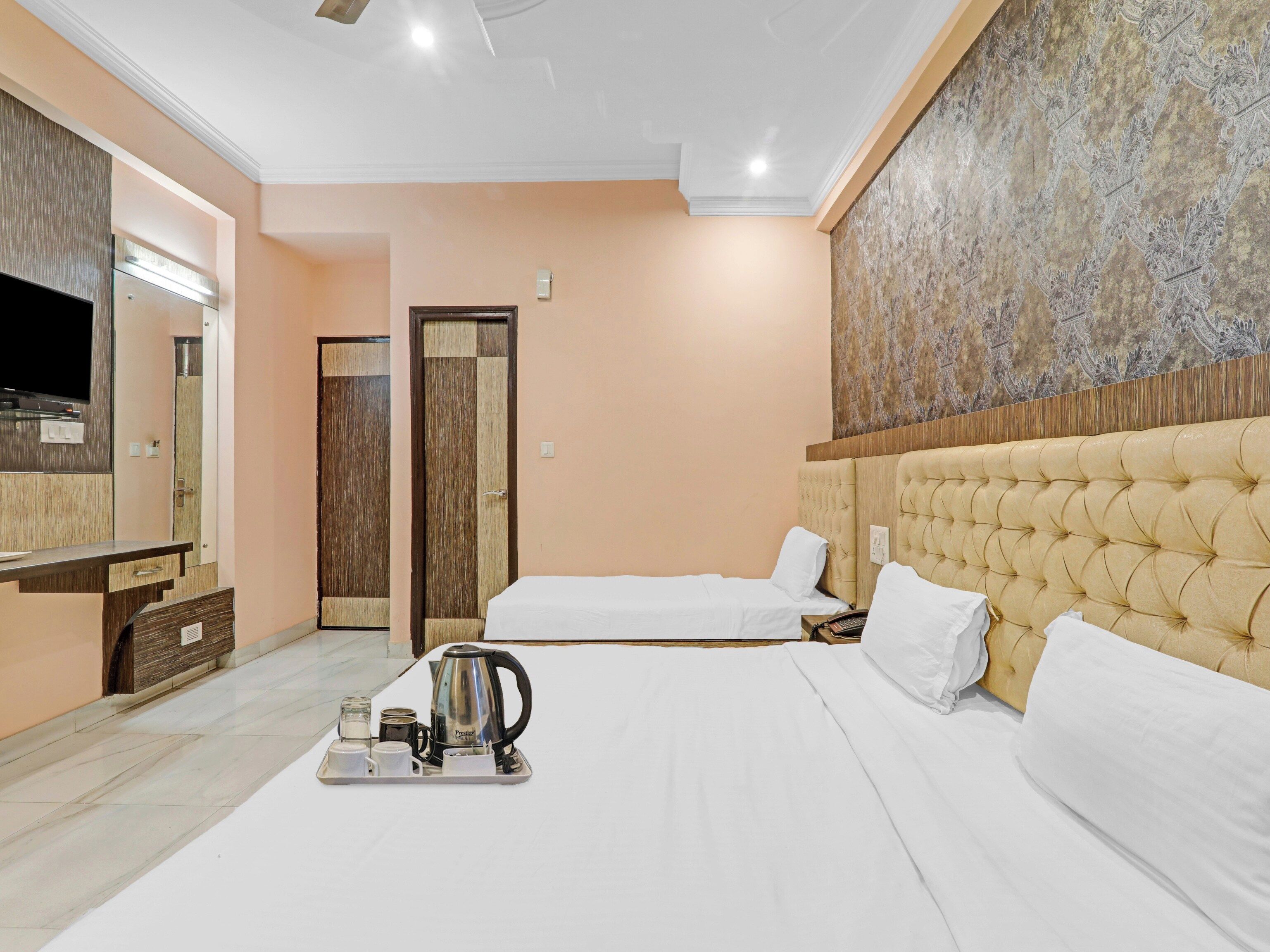 A hotel room with two beds, a minibar, a television, and a large decorative wall.