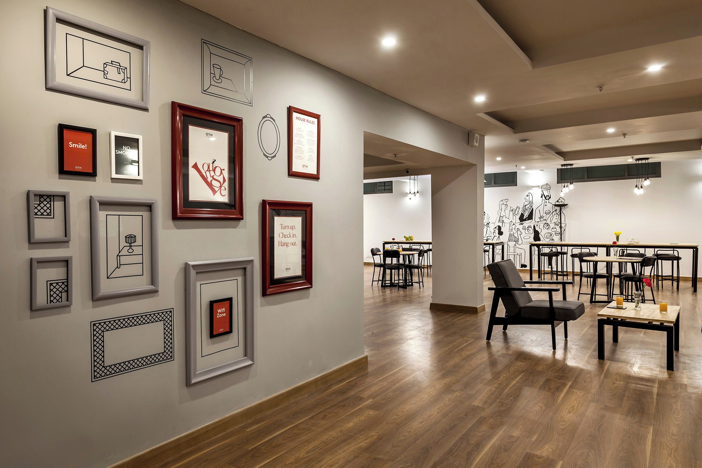 A modern interior with framed artwork on the walls, a dining area with tables and chairs, and a wooden floor.