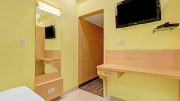 A room with a bed, a desk, a mirror, a television, and a door leading to another room.