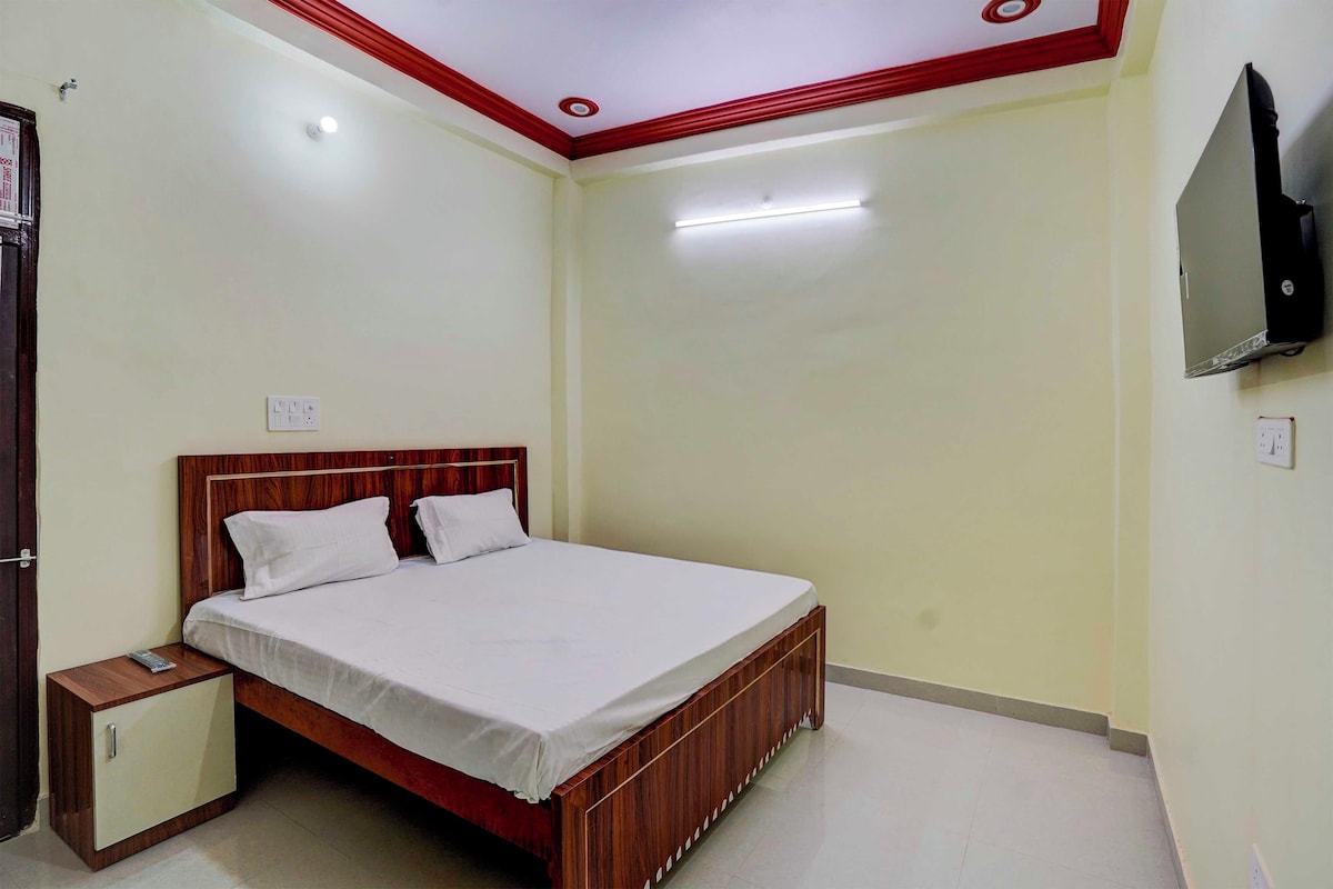 Un dormitorio con una cama de madera, una mesita de noche, un televisor montado en la pared y una puerta.