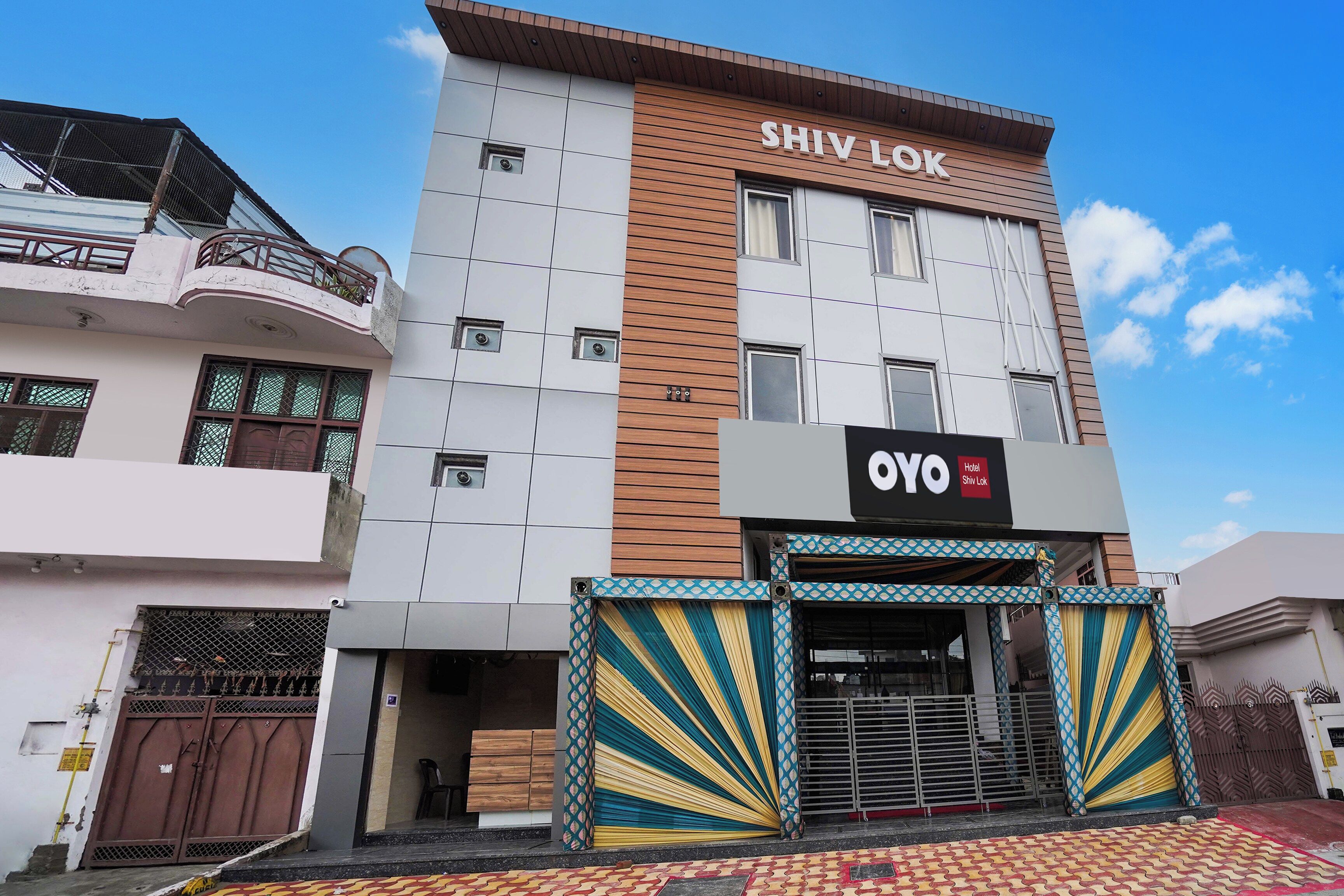 A hotel named Shiv Lok with a modern facade, a prominent sign, and a gated entrance.