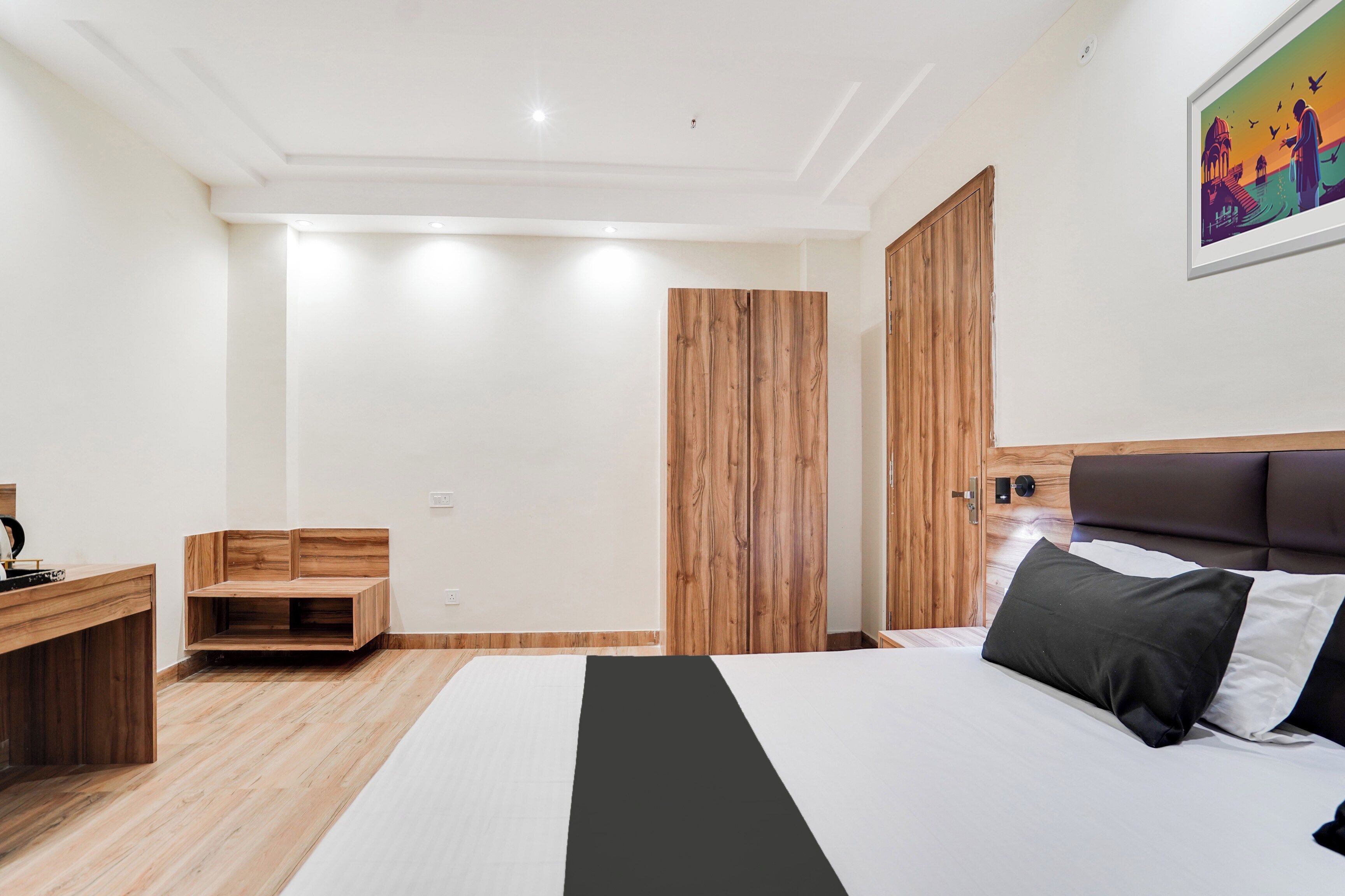A modern bedroom with a bed, a wooden wardrobe, a bedside table, and a wall-mounted artwork.