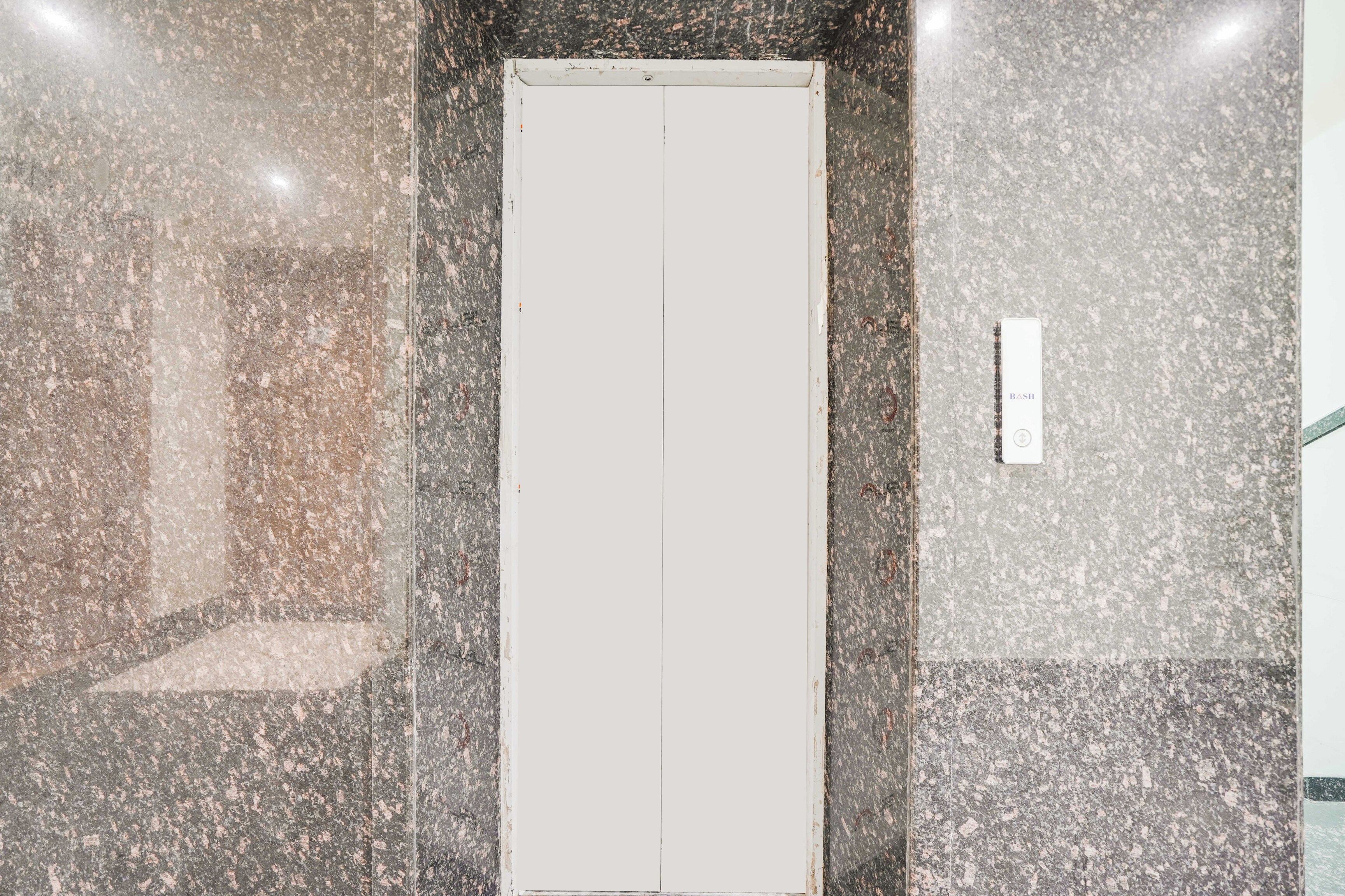 A corridor with a white door, granite walls, and a small rectangular object on the wall.
