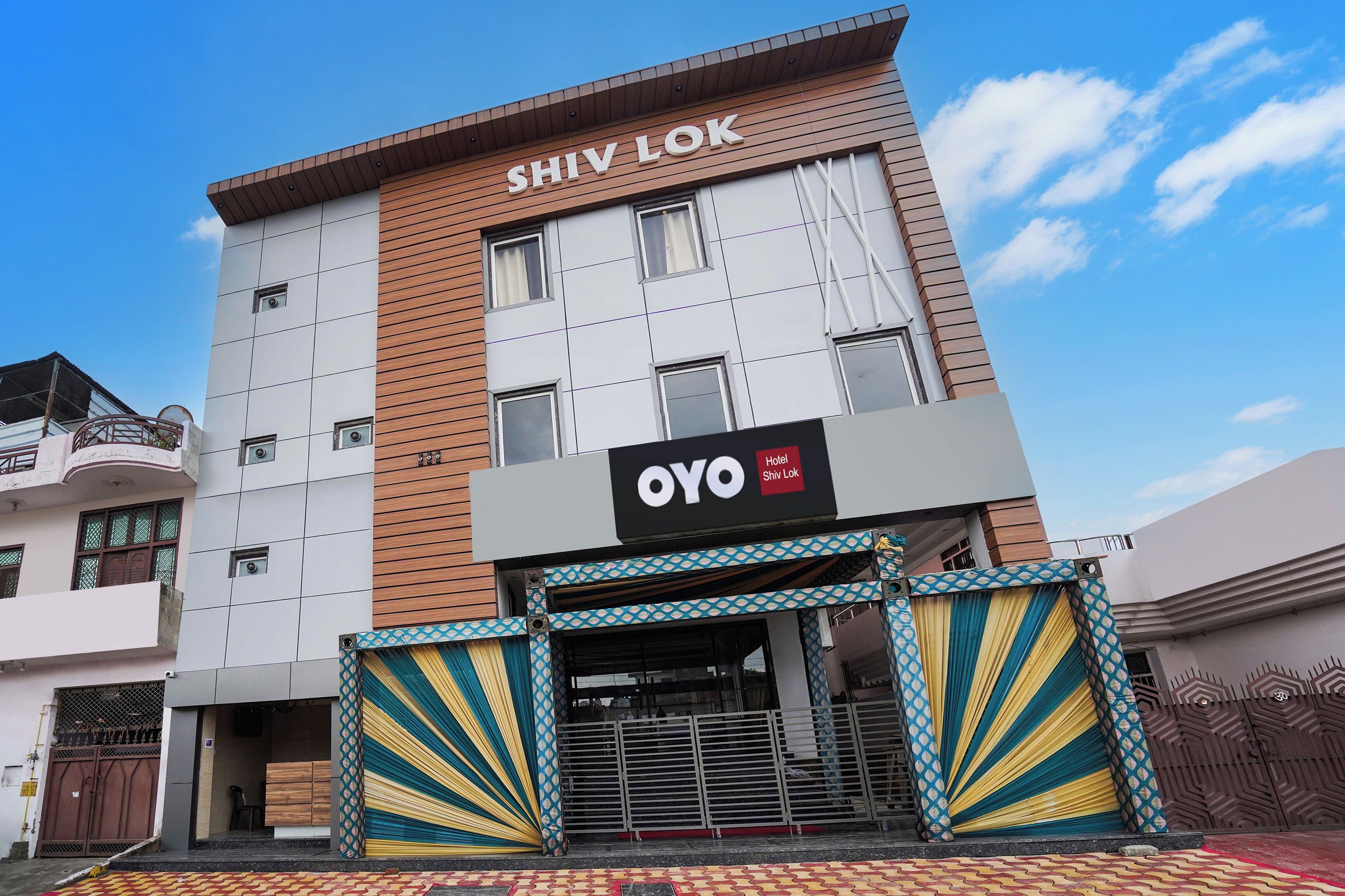 Hotel Shiv Lok med en moderne facade, et tydeligt skilt og en indgang med et mønster.