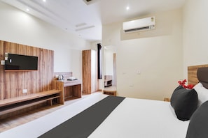 Ein modernes Hotelzimmer mit einem großen Bett, einem Flachbildfernseher an einer Holzwand, einer kleinen Küchenzeile und einer Klimaanlage.