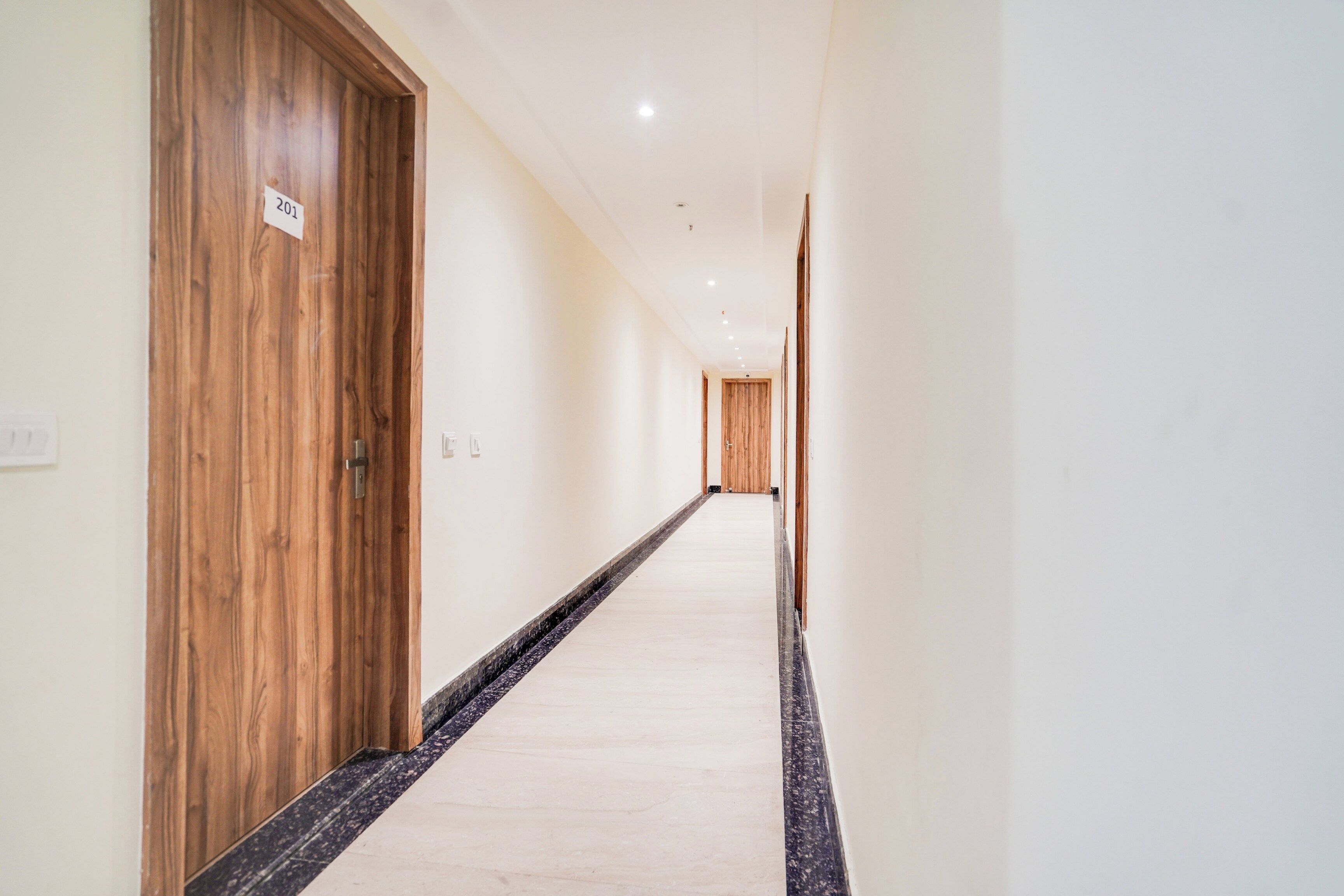A hotel corridor with wooden doors, a marble floor, and a white wall.