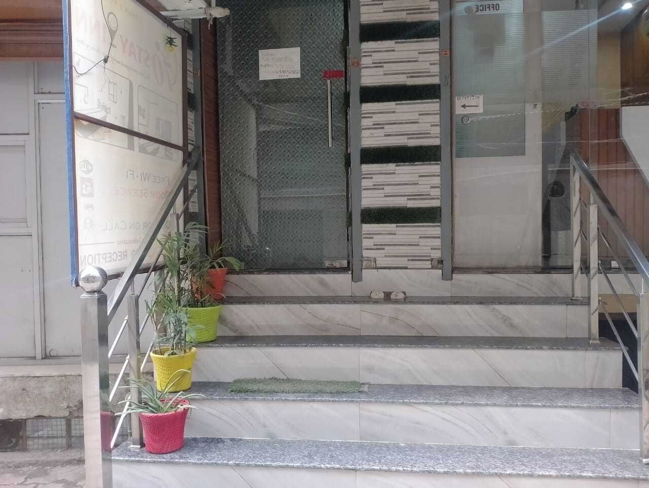 Un escalier menant à l’entrée d’un immeuble, avec des rampes en métal et des plantes en pot à sa base.