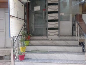 Una escala que condueix a l'entrada d'un edifici, amb baranes metàl·liques i plantes en testos a la base.