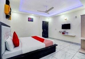 Una habitación de hotel con cama, ventilador de techo, televisión y una puerta.