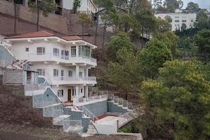 Un edificio de varios pisos con una escalera que lleva a un balcón, rodeado de árboles.