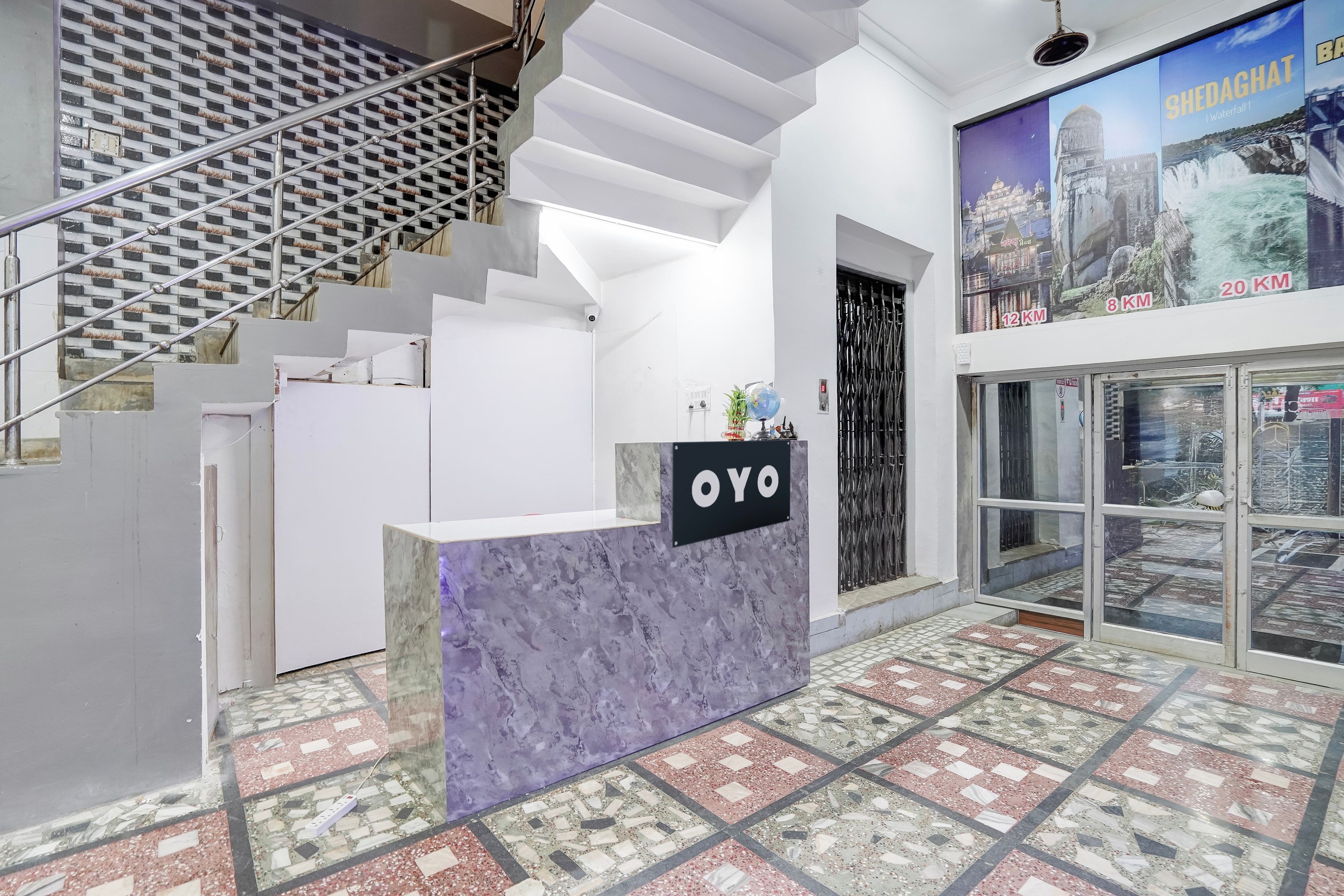 A reception desk with a sign reading 'OYO' in a modern interior with a patterned floor and a staircase.