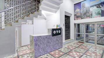 A reception desk with a sign reading 'OYO' in a modern interior with a patterned floor and a staircase.