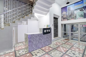 A reception desk with a sign reading 'OYO' in a modern interior with a patterned floor and a staircase. - Hotel O City View (Jabalpur)