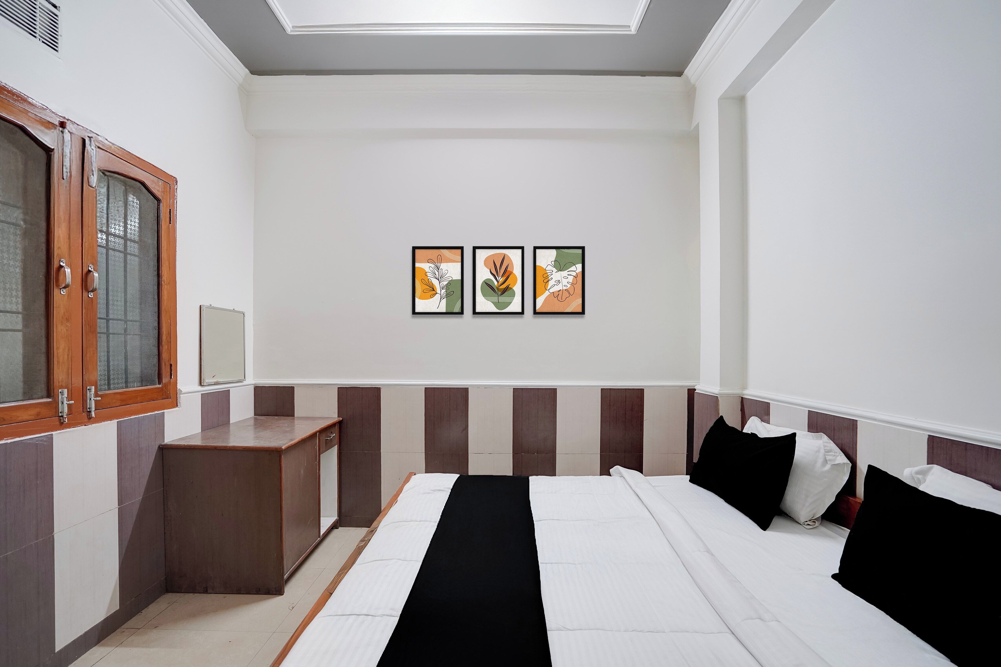 A hotel room with a bed, bedside table, wardrobe, and three framed artworks on the wall.