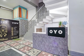 Un espace d’accueil doté d’un comptoir en marbre, d’un escalier avec une rampe en métal et d’une armoire aux couleurs vives.