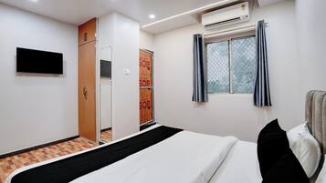 A hotel room with a bed, an air conditioning unit, a window with curtains, a wardrobe, and a flat-screen TV mounted on the wall.