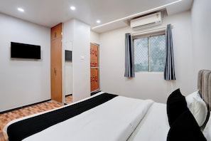 Une chambre d’hôtel équipée d’un lit, d’un climatiseur, d’une fenêtre avec des rideaux, d’une armoire et d’un téléviseur à écran plat fixé au mur.