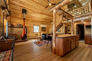 A log cabin interior with a central fireplace, wooden staircase, and a cozy seating area. - Kent's Knoll - Inspired by the iconic landscape of the Black Hills. (Newcastle)
