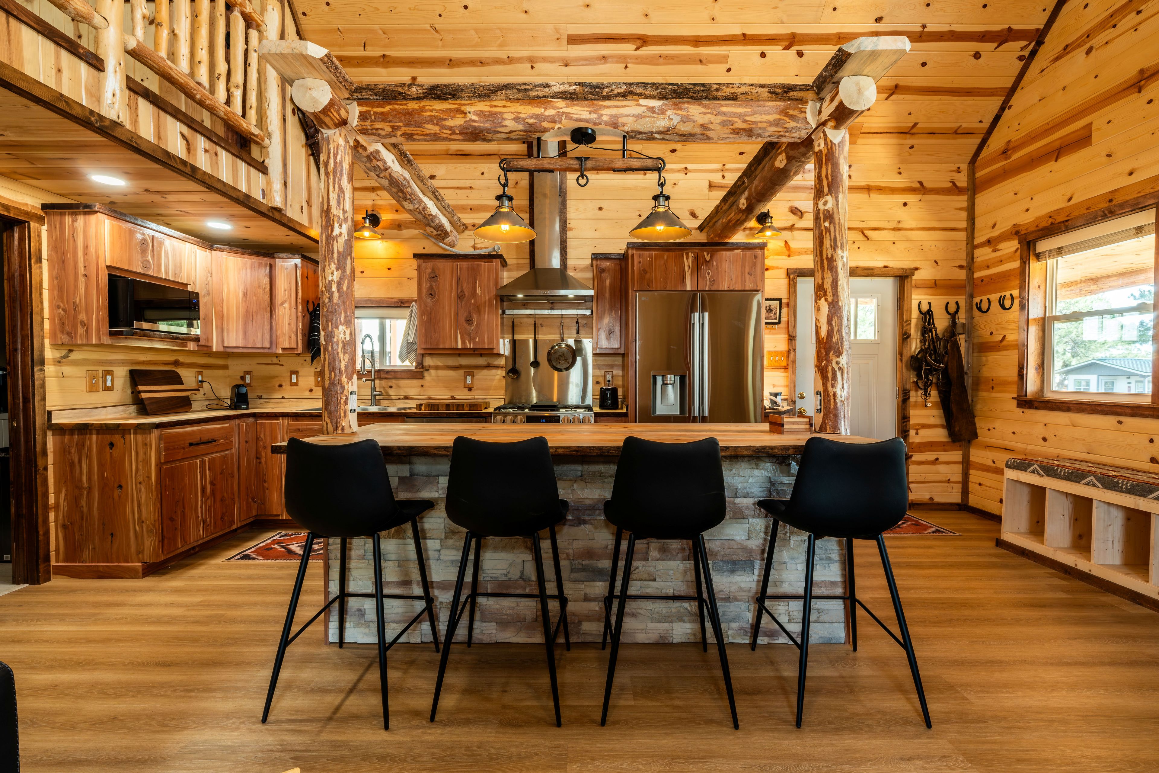 Un interior rústico de madera con una barra central tipo isla, taburetes negros y un refrigerador de acero inoxidable grande.