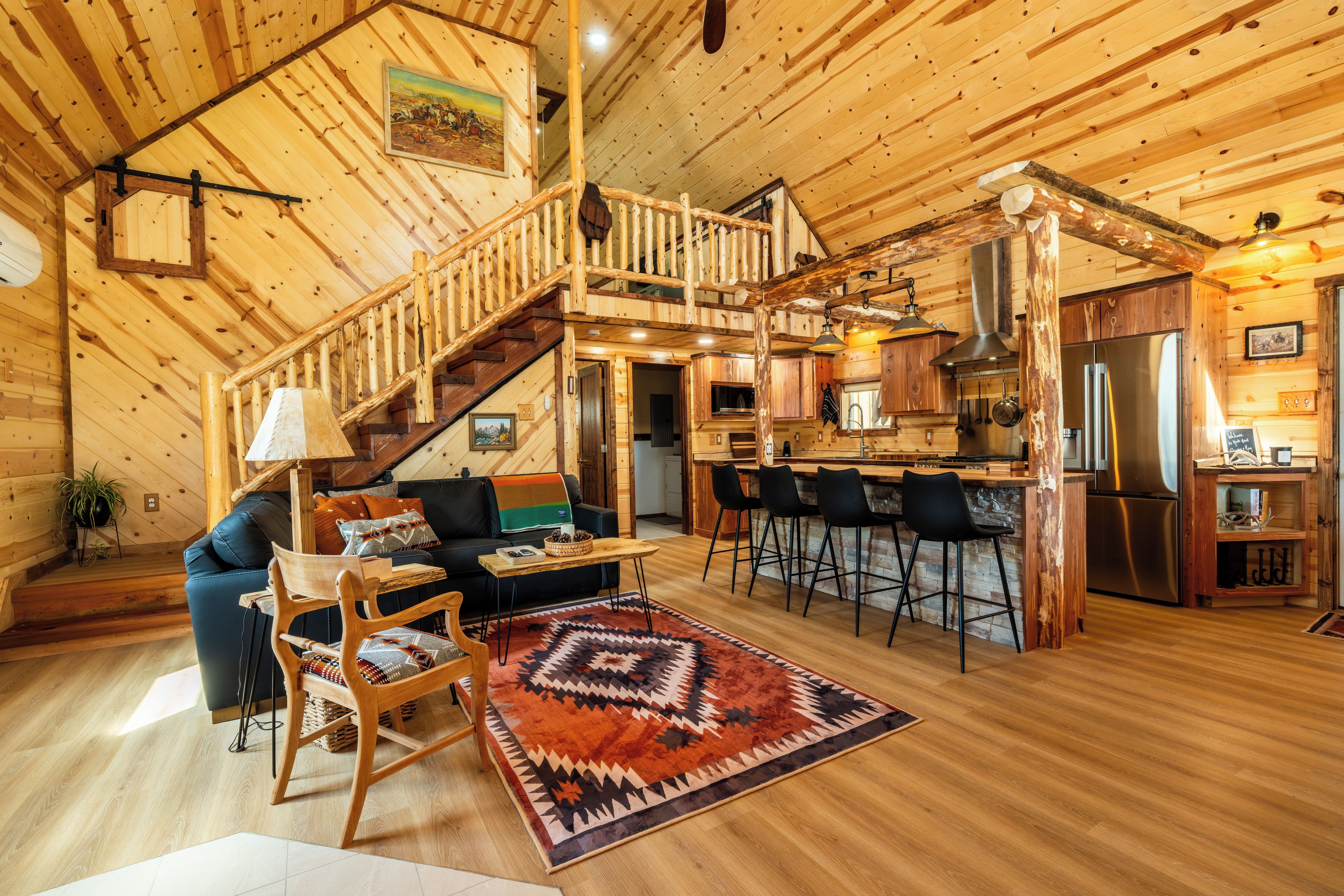 Un interior de madera con una escalera, una sala de estar con sofá y sillones, una cocina con barra y un comedor.