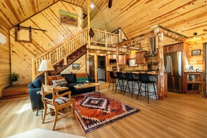 A wooden interior with a staircase, a living area with a sofa and chairs, a kitchen with a bar, and a dining area. - Kent's Knoll - Inspired by the iconic landscape of the Black Hills. (Newcastle)