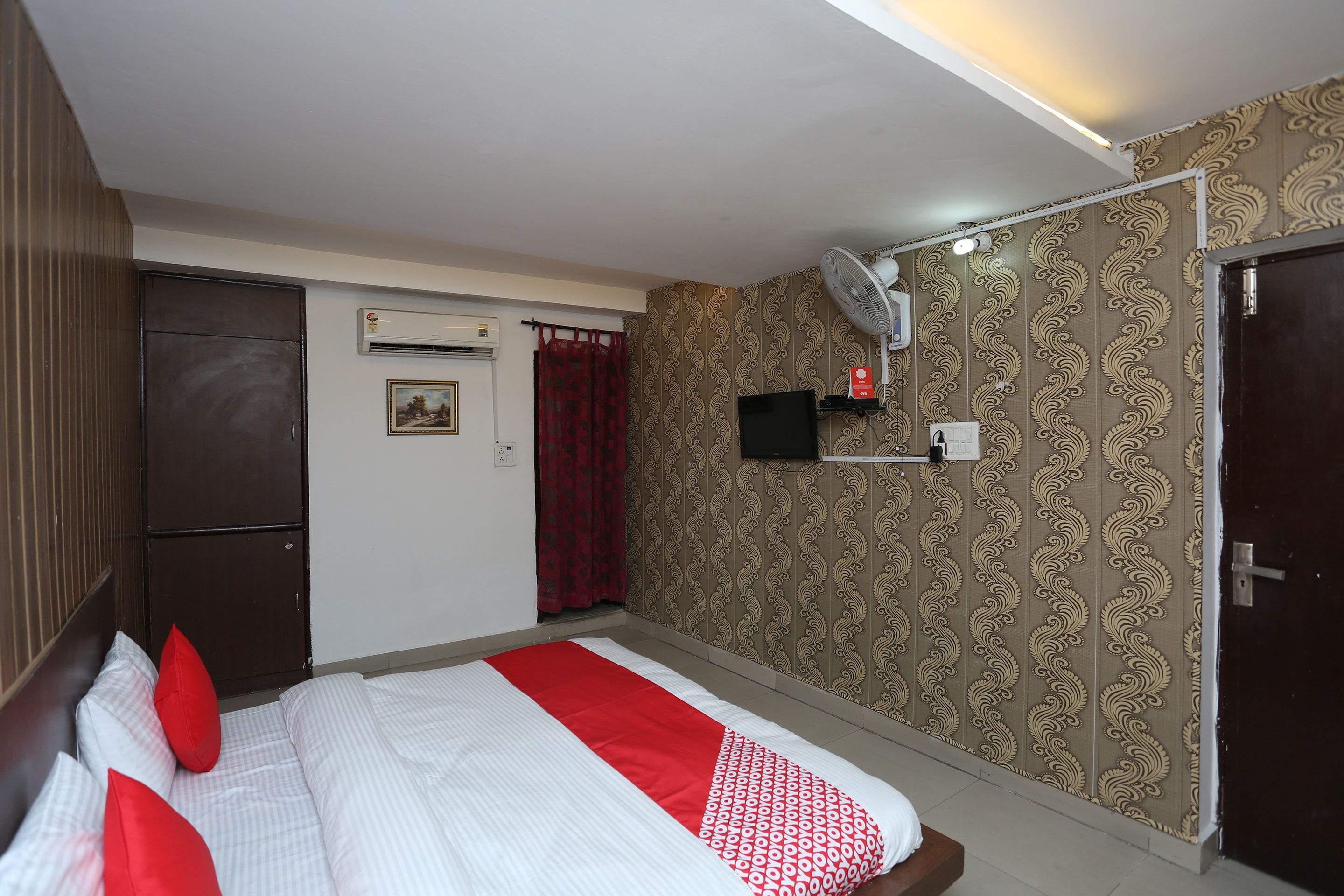 A hotel room with a bed, an air conditioning unit, a television, and a door.