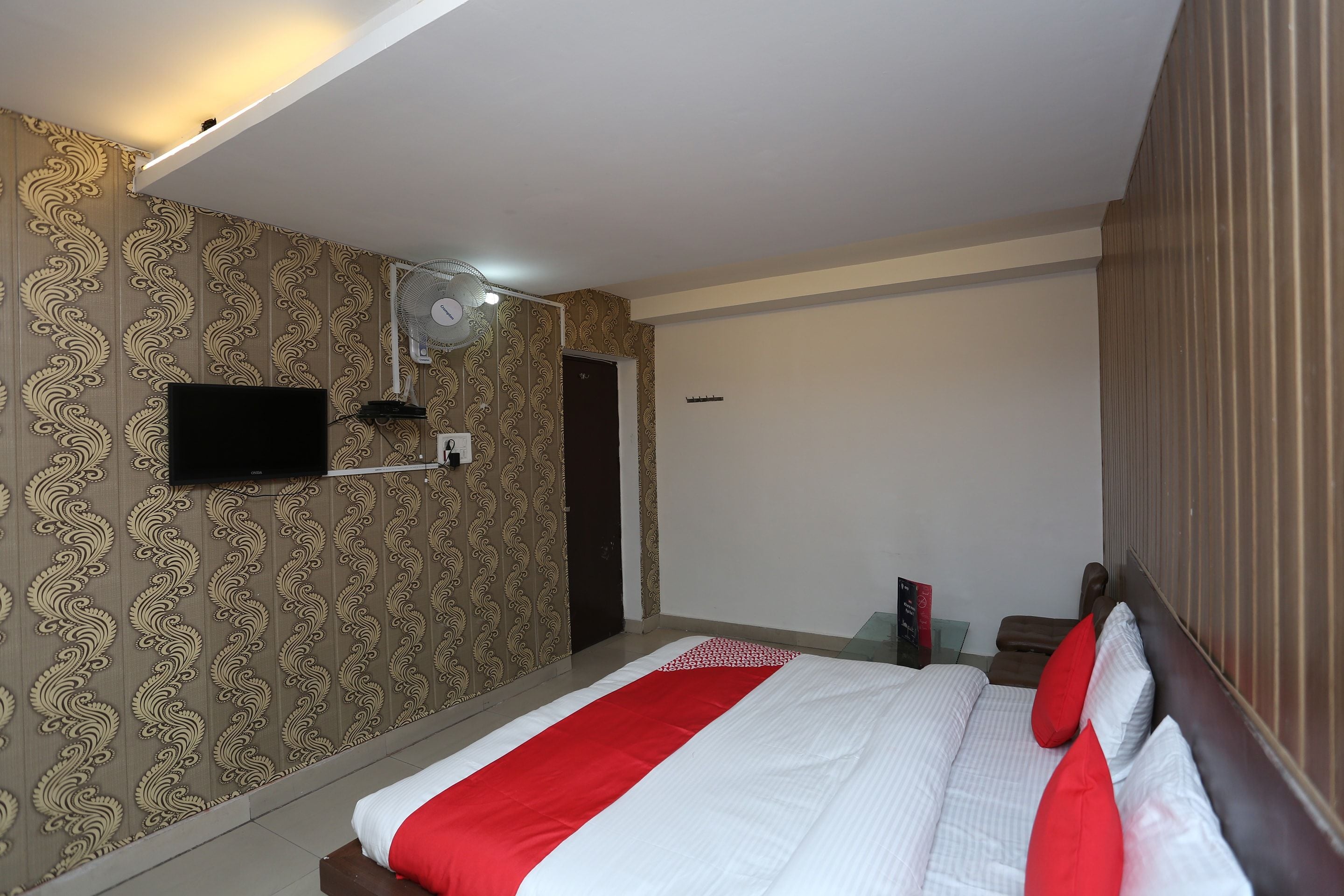 A hotel room with a bed, a television mounted on the wall, and a door.