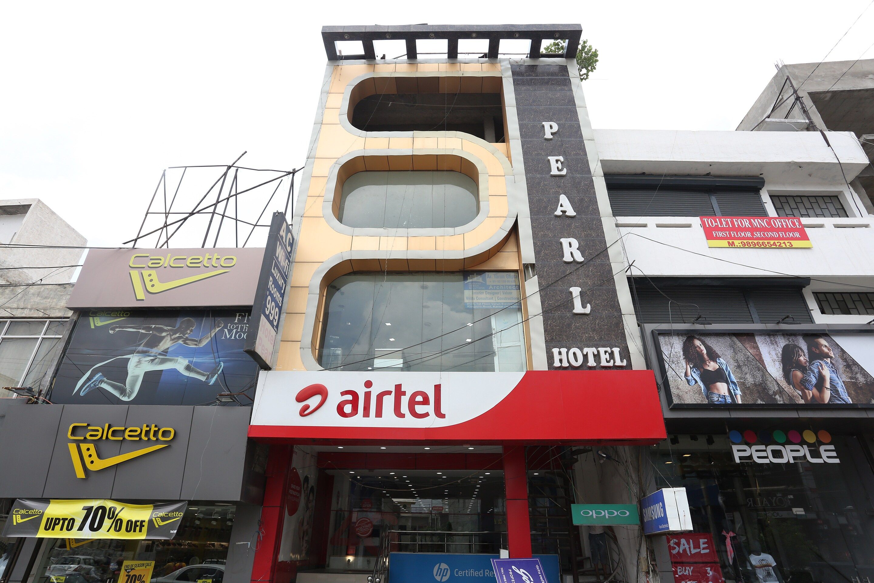 Un hotel con un llamativo letrero de 'Airtel', un letrero de 'Pearl Hotel' y varios otros letreros de negocios, incluyendo 'Caletto' y 'People'.