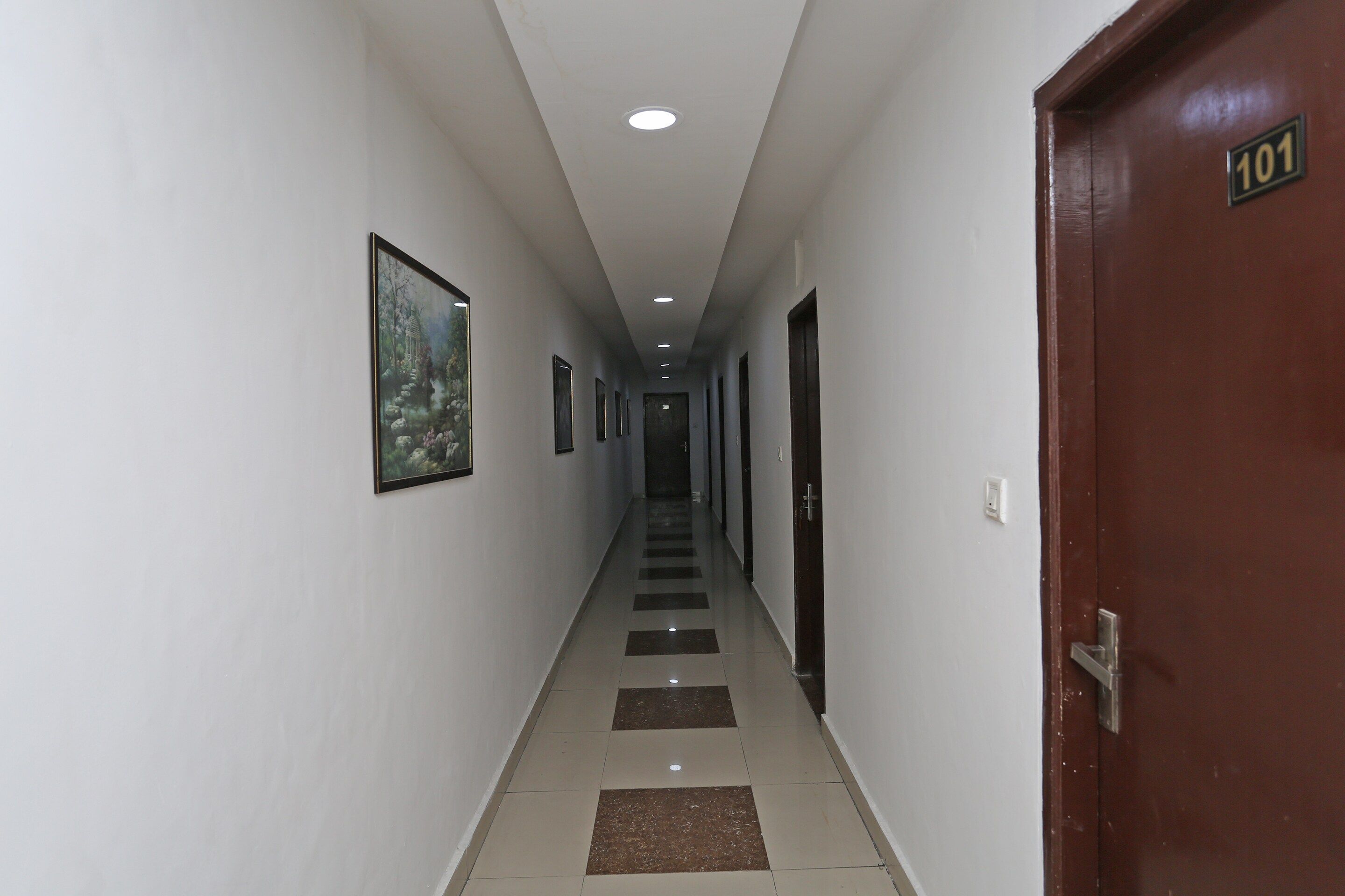 A corridor with a tiled floor, framed pictures on the walls, and a door marked with the number 101.