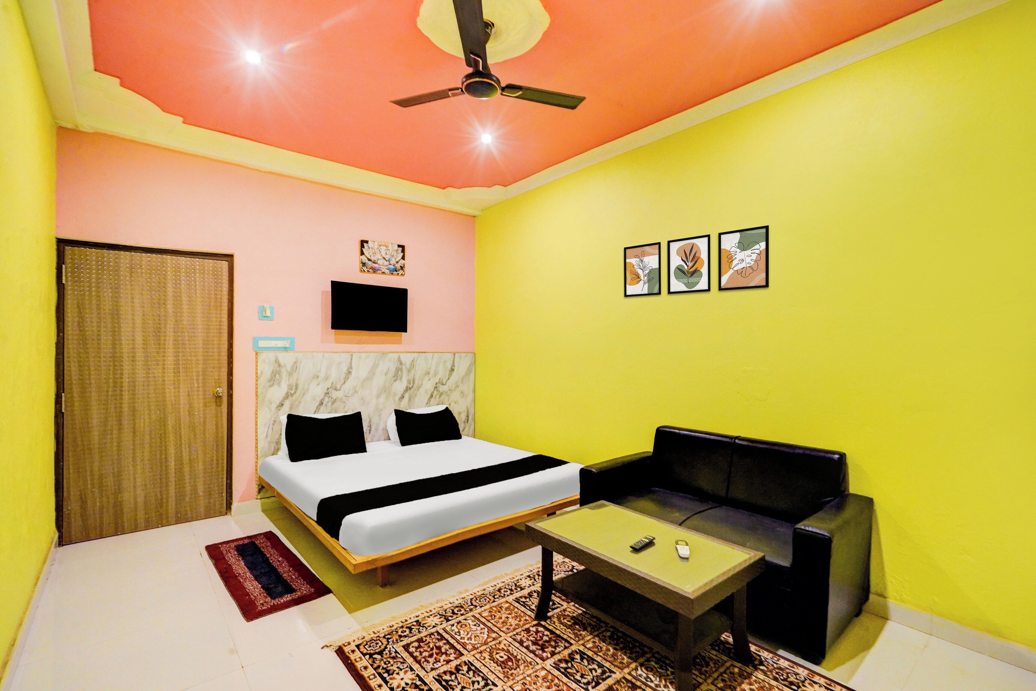 Quarto com cama, sofá, ventilador de teto, TV e obras de arte na parede.