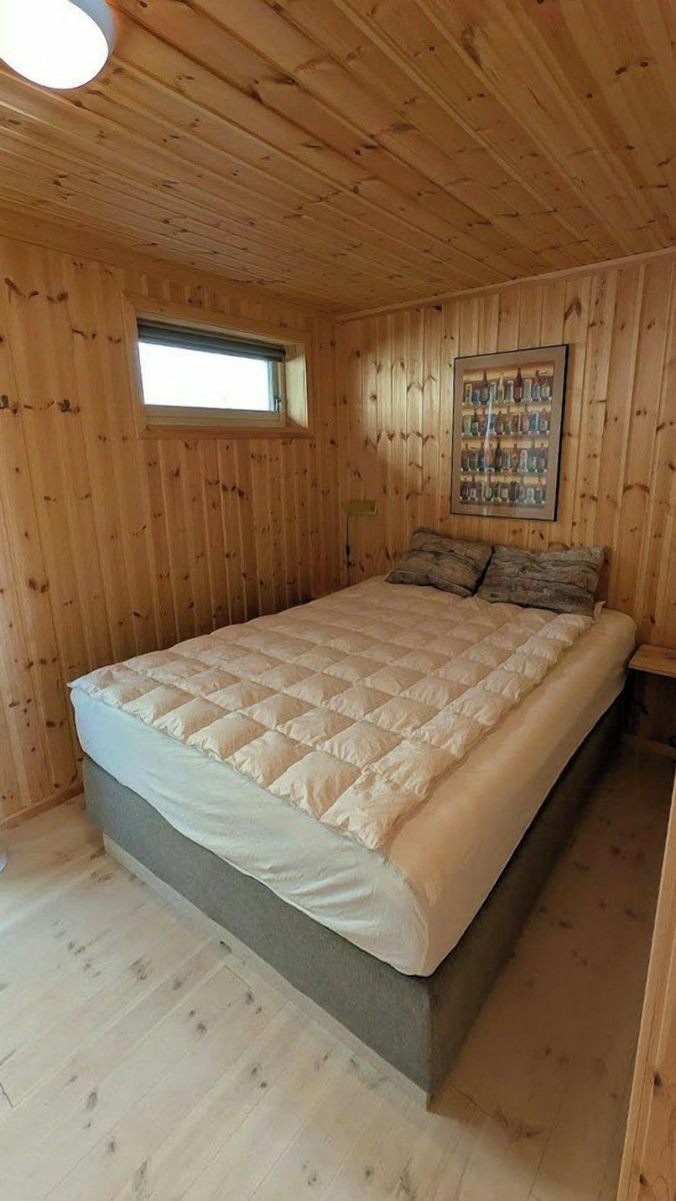 Une pièce aux murs lambrés, avec un lit, une fenêtre et un tableau encadré.