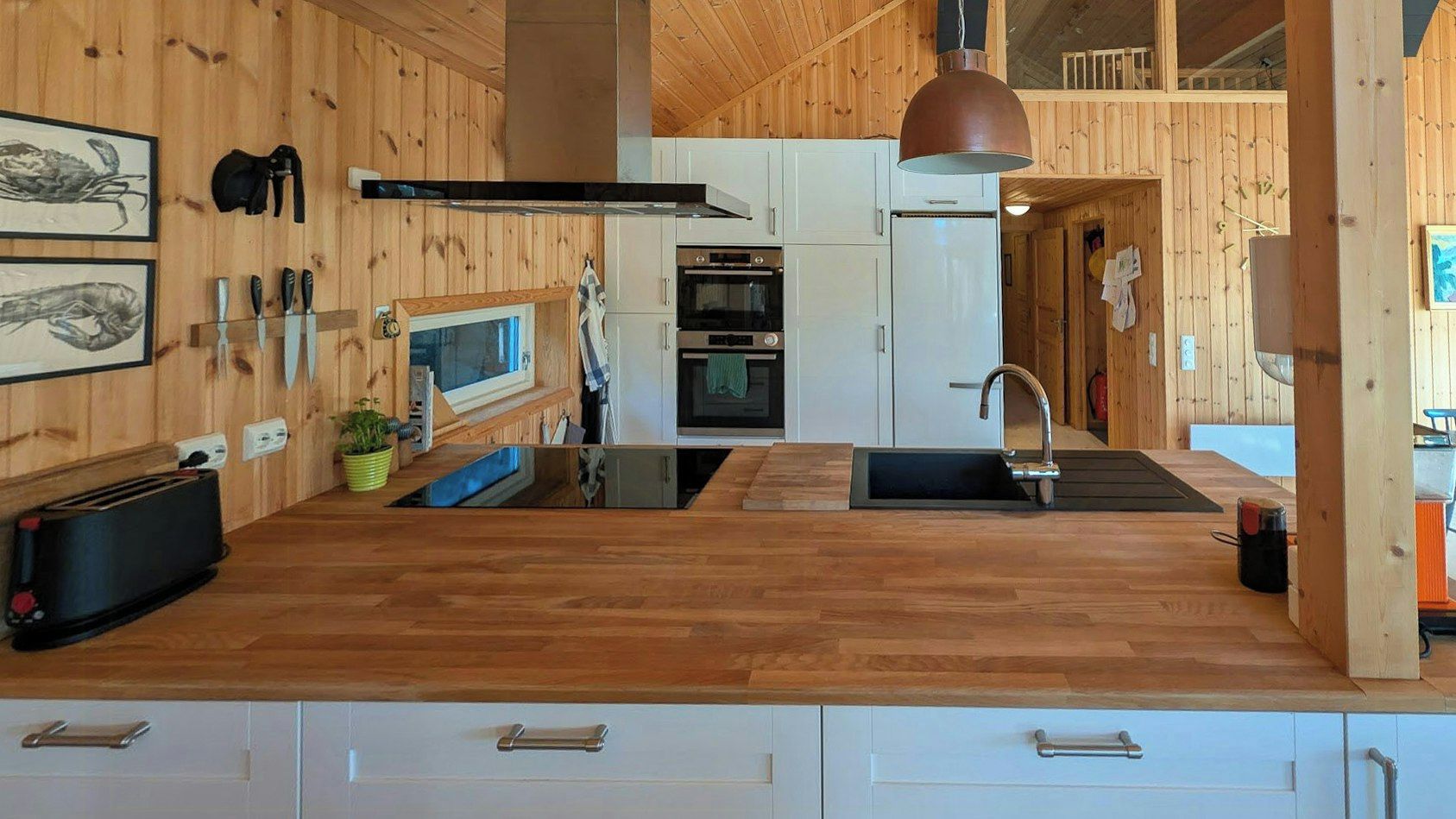 A modern kitchen with wooden cabinetry, a central island, and a hanging pendant light.