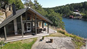 Una baita con una veranda che si affaccia su un lago, ampie finestre e un camino.