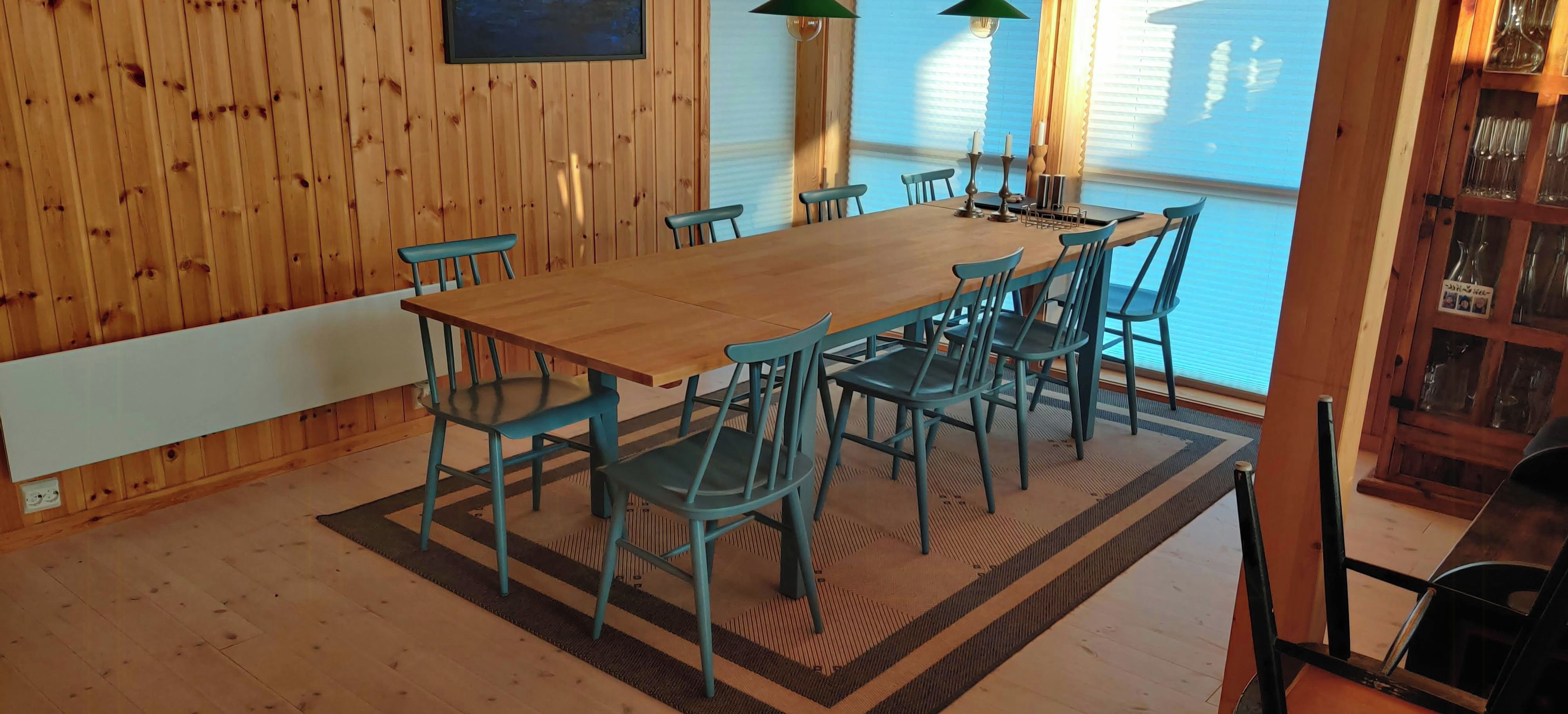 Una habitación con paneles de madera, una mesa grande con sillas, una ventana con persianas y una estantería con cristalería.