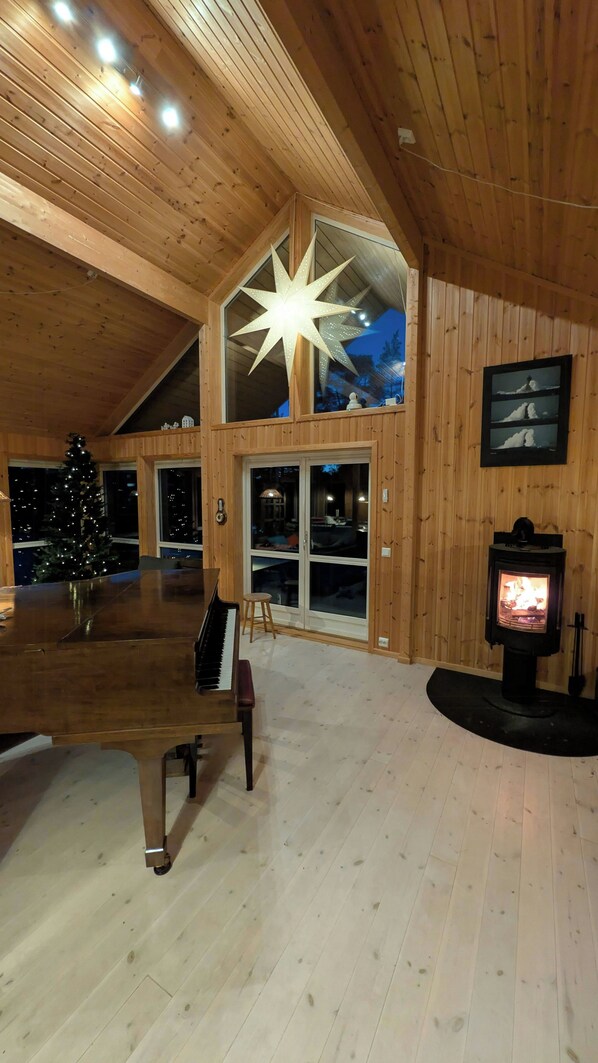 Una camera spaziosa con soffitto in legno, un'ampia lampada a forma di stella, un pianoforte, un albero di Natale e una stufa a legna.