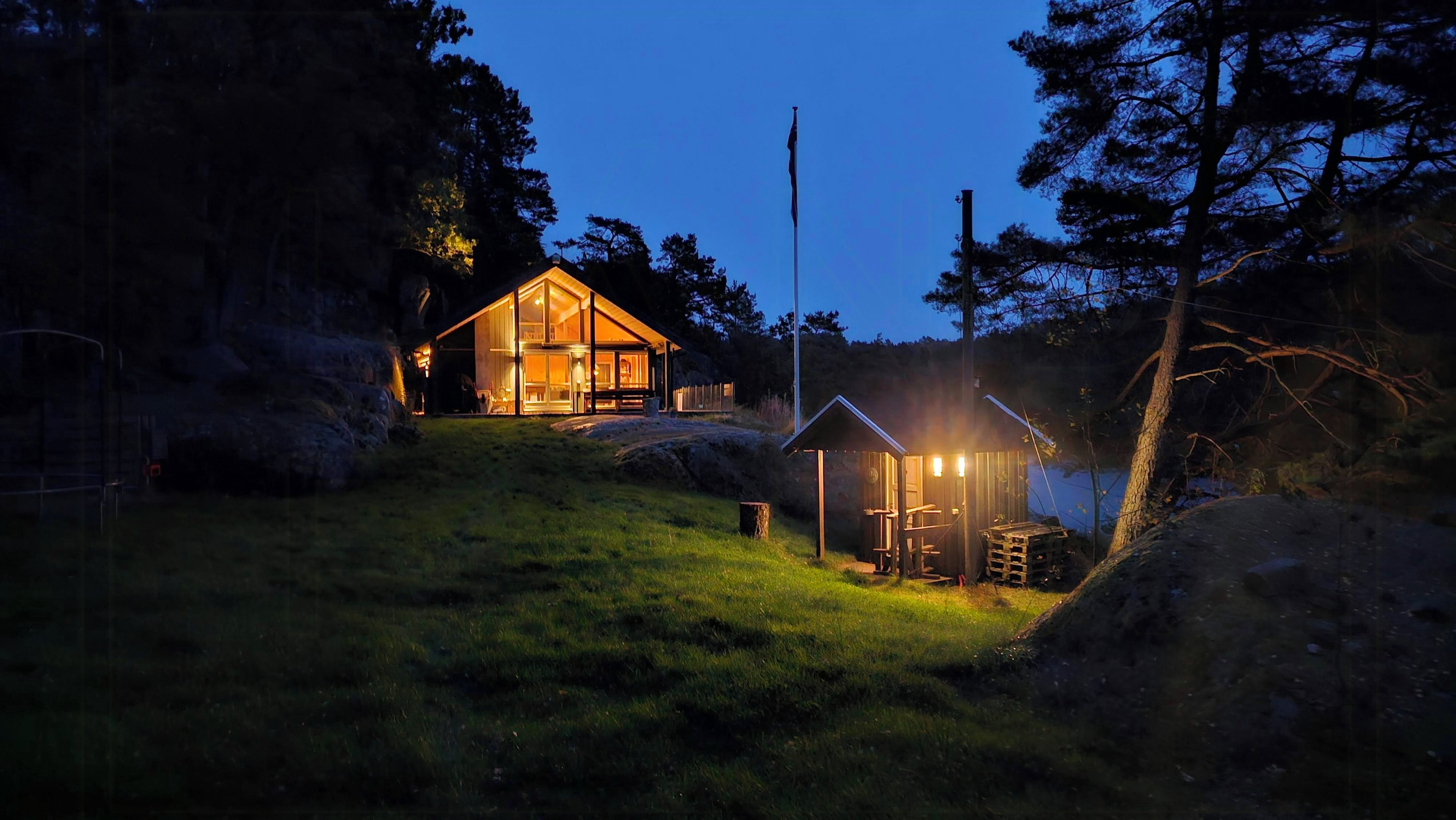 Une cabane dotée d’une grande fenêtre et d’une petite structure attenante, entourée d’arbres et d’une zone herbeuse.