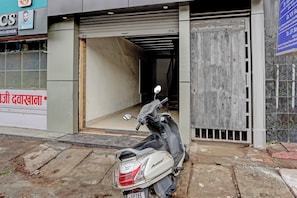 A scooter parked in front of a building with a closed shutter and a signboard with text. - Hotel O by OYO Skycity (Kanpur)