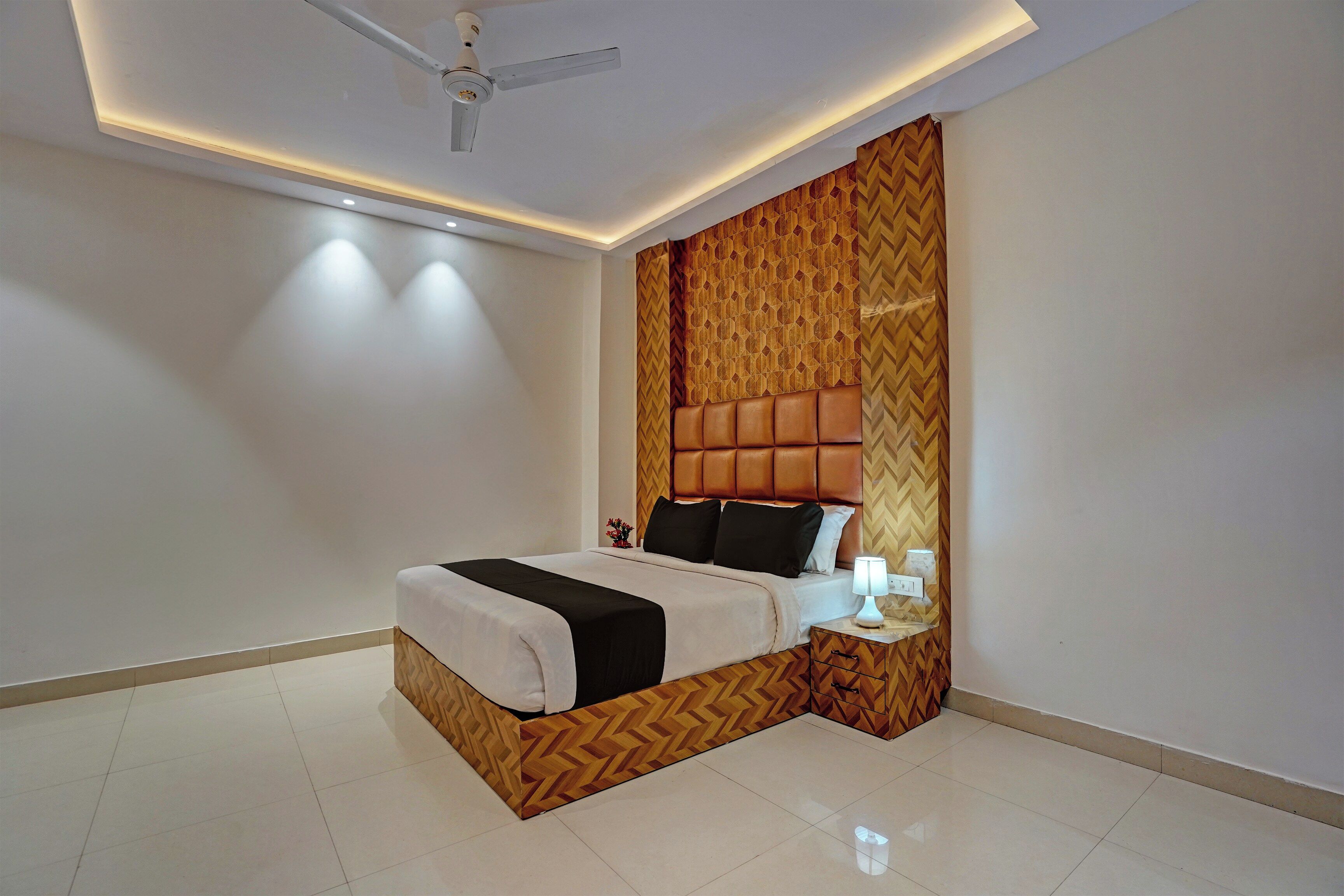 Une chambre à coucher moderne avec un lit, une table de chevet, un ventilateur de plafond et un mur orné d’un motif géométrique.