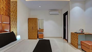 A hotel room with a bed, a desk, a mirror, and an air conditioning unit.