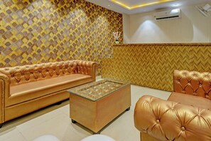 A room with a patterned wall, a leather sofa, a glass coffee table, and an air conditioning unit. - Hotel O by OYO Skycity (Kanpur)