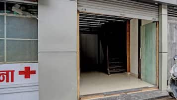 A closed storefront with a metal shutter door, a visible window with a red cross sign, and a scooter parked outside.