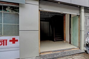 Una tienda cerrada con un portón metálico, un ventanal con un letrero de cruz roja, y una moto estacionada afuera.