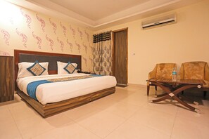 Ein Hotelzimmer mit einem Bett, einem Tisch, zwei Stühlen, einer Klimaanlage und einem Vorhang mit Baummuster.